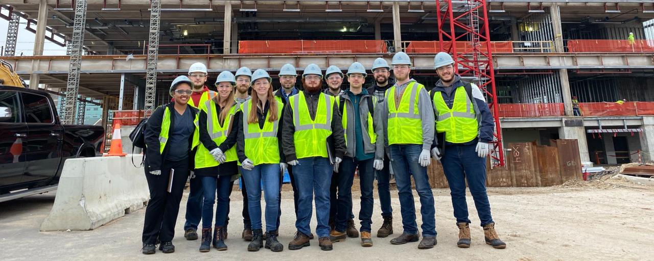 Group of students with hard hats on in front of a construction building